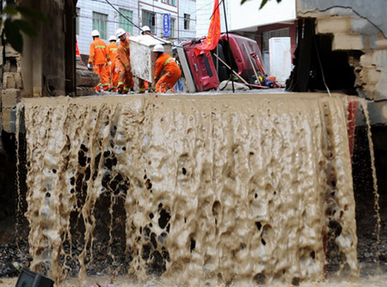 Rescuers clear debris on the street on Wednesday after rainstorms hit Xiaohe township in Qiaojia county, Yunnan province. A dozen people were killed and about 30 remain missing after the flooding. [Xinhua]