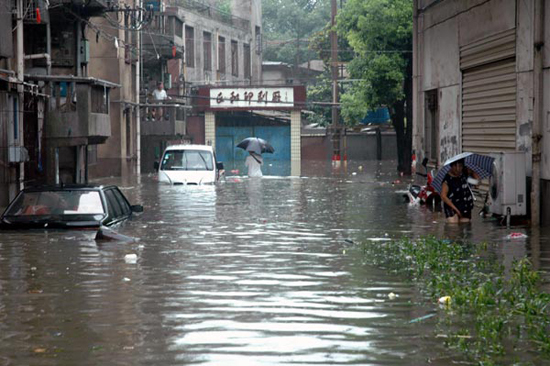 A man holding an umbrella is seen in a flooded residential community in Anqing, Anhui province, on July 13. [Photo/Xinhua]