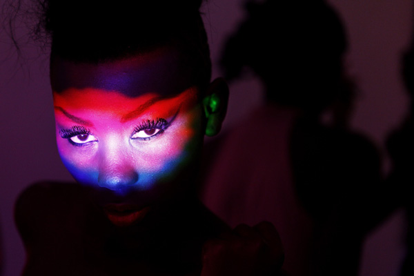 Coloured lights are reflected onto the face of model Sira Sissokno as she waits backstage during Dakar Fashion Week July 16, 2010. Picture taken July 16, 2010.(