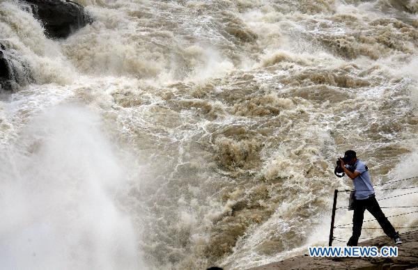 A tourist takes photos of the spectacular torrents of the Hukou Waterfall on the Yellow River, resulting from upriver precipitation, near Jixian County, northern China's Shanxi Province, July 17, 2010. [Xue Jun/Xinhua]