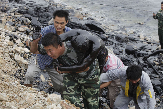 Workers try to save a pair of colleagues from going under a thick blanket of oil. The pair were trying to fix an underwater pump on a pipeline which exploded last week pouring 1,500 tonnes of crude into the sea. [163.com]