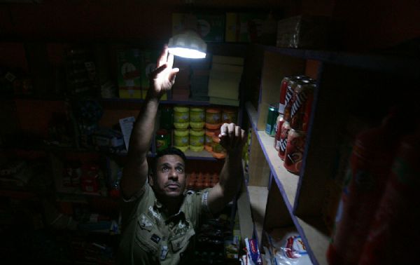 An Iraqi grocer fixes a lamp with a rechargeable battery in his shop during power outage in Baghdad on June 30, 2010. Private power providers in Baghdad are selling electricity at almost four times the maximum legal price, exploiting shortages and stifling summer heat while crime bosses pilfer dwindling public supplies.[yeeyan.org]