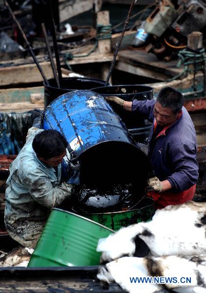 Workers transport crude oil during the oil spill cleanup operation near Xingang Harbor in Dalian City, northeast China's Liaoning Province, July 25, 2010.