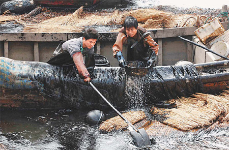 Two workers clean up an oil spill at a fishing port off Dalian, Liaoning province, where two oil pipelines exploded on July 16. Cleanup efforts have successfully contained the spill from entering international waters, Dalian Vice-Mayor Dai Yulin said at a press conference on Monday. [Xinhua] 