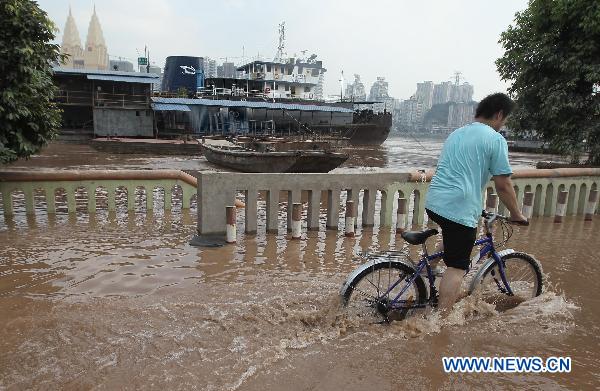 A resident pulls the bike forward in Binjiang Road submerged by floodwaters in Chongqing, southwest China, July 27, 2010. Though just dried off, parts of the city were submerged again on Tuesday due to the rising water level of the Yangtze River. [Xinhua]