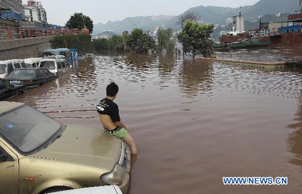 A resident sits on a car in Binjiang Road submerged by floodwaters in Chongqing, southwest China, July 27, 2010. Though just dried off, parts of the city were submerged again on Tuesday due to the rising water level of the Yangtze River. [Xinhua]