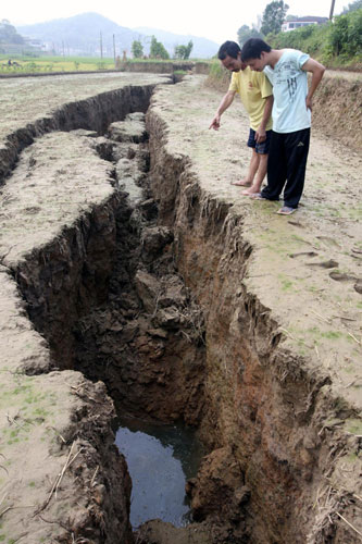 Two men look at fissures in the ground in Hutang village of Loudi, Central China's Hunan province, July 28, 2010.