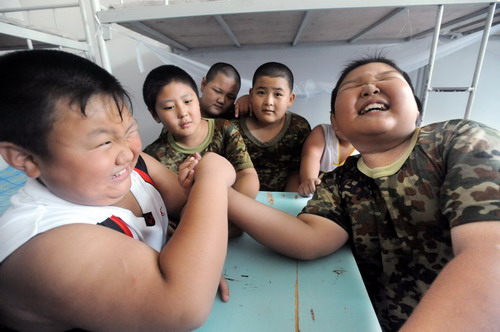 Two boys hand-wrestle during a break at the training camp in Shenyang, capital of northeast China&apos;s Liaoning province on July 29, 2010. Over 100 chubby boys from various cities in China attend a special weight-losing program in the city Thursday. The 20-day program combines methods of military training with guidance from health experts. Children will train their bodies and eat a tailor-made healthy menu.[Xinhua]