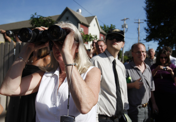 A woman in a crowd of on-lookers uses a pair of binoculars to scan a crowd of guests loading onto a bus heading for Chelsea Clinton's wedding in Rhinebeck, New York July 31, 2010.