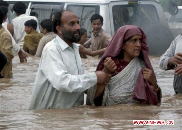 People walk through the waterlogged street in northwest Pakistan&apos;s Pabbi on Aug. 1, 2010. The current horrible wave of floods and landslides triggered by torrential monsoon rains has killed more than 900 people in Pakistan while 1 million people have become homeless as the flood is now hitting western and southern parts of the country.[Saeed Ahmad/Xinhua]