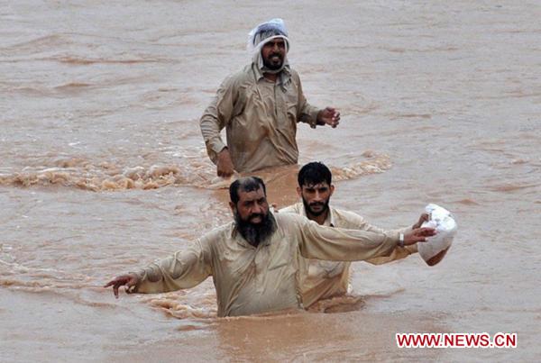 People walk through the waterlogged street in northwest Pakistan&apos;s Pabbi on Aug. 1, 2010. The current horrible wave of floods and landslides triggered by torrential monsoon rains has killed more than 900 people in Pakistan while 1 million people have become homeless as the flood is now hitting western and southern parts of the country. [Saeed Ahmad/Xinhua]