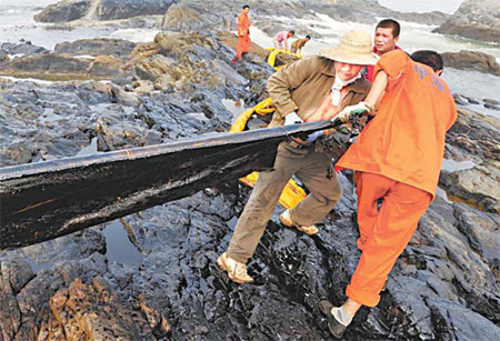 Workers relocate an oil obstruction belt which was washed ashore in Dalian bay, Liaoning province, last Thursday. [China Daily] 