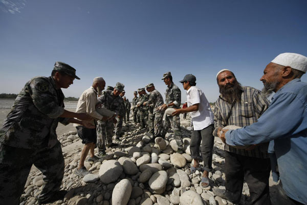 Paramilitary policemen and local residents pass stones used to strengthen a dyke in Hotan county of Northwest China&apos;s Xinjiang Uygur autonomous region, August 3, 2010. 