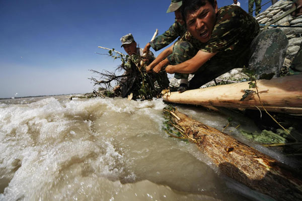 Paramilitary policemen use trees to strengthen a dyke in Hotan county of Northwest China&apos;s Xinjiang Uygur autonomous region, August 3, 2010. [Xinhua]