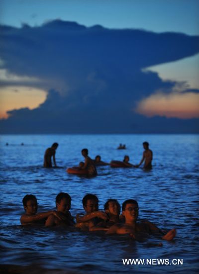 Photo taken on Aug. 4, 2010 shows people relaxing in the sea in Haikou, capital of south China&apos;s Hainan Province. As heat keeps on, coastlines covered by sunset glow become a hot spot for redidents to cool down themselves in summer. [Xinhua]