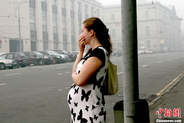 A pregnant woman wears a mask to protect herself from the smell of heavy smog, caused by peat fires in nearby forests, as she waits for a bus at a bus station in central Moscow, August 6, 2010. [Chinanews] 