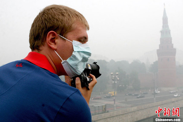 A photographer wears a mask to protect himself from the smell of heavy smog, caused by peat fires in nearby forests, as takes photos in central Moscow, August 6, 2010. [Chinanews] 