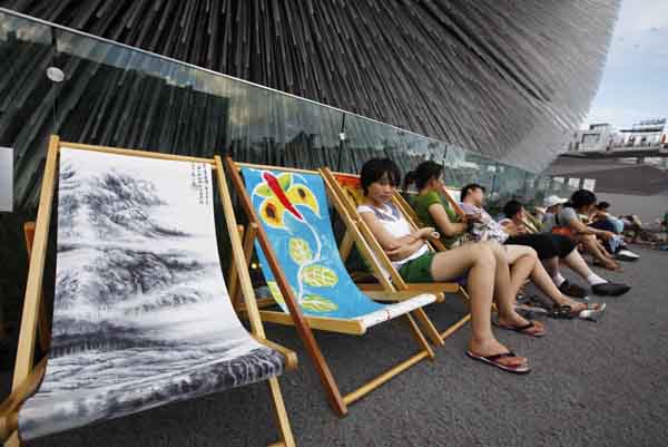 People rest on chaise longues near the Britain Pavilion in 2010 World Expo Site in Shanghai, China, Aug. 6, 2010. Painted chaise longues designed by famous designers from Britain and China were brought to Expo recently. [Xinhua]