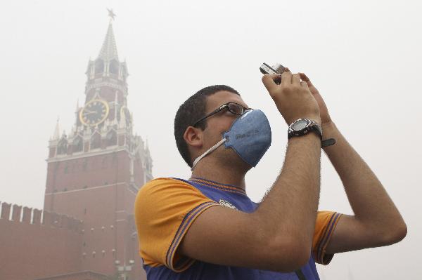 A tourist, wearing a mask to protect himself from the smell of heavy smog caused by peat fires in nearby forests, takes a picture as he walks along Red Square in central Moscow August 9, 2010.[Xinhua]