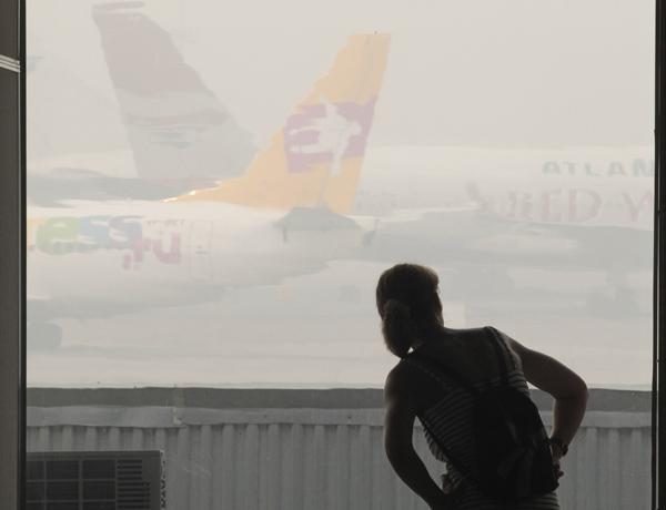 A passenger looks at airplanes shrouded in heavy smog, caused by peat fires in nearby forests, at Vnukovo airport outside Moscow, August 9, 2010. [Xinhua]