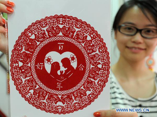 A woman shows a paper-cutting made by local folk artists to celebrate the upcoming 'Qixi', the Chinese Valentine's Day, in Suzhou, east China's Jiangsu Province, Aug. 8, 2010. Paper-cuttings on the theme of romantic love are quite popular among residents and tourists in Suzhou.
