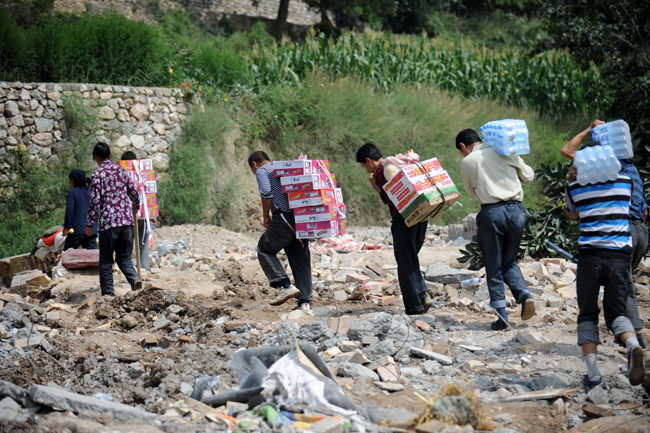 Residents of Yuanyue Village carry home relief materials in the landslides-hit Zhouqu County, Gannan Tibetan Autonomous Prefecture in northwest China&apos;s Gansu Province, Aug. 10, 2010. The rain-triggered landslide has caused 337 people dead and 1,148 others missing till 2:00 p.m. (0600 GMT) Monday. [Xinhua]