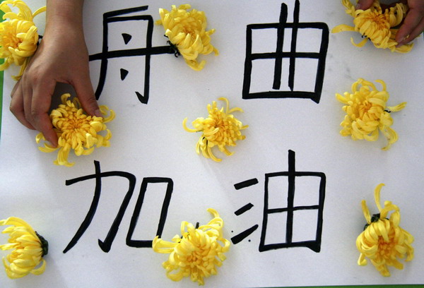 Yellow chrysanthemum flowers are seen at a &apos;Zhouqu, come on&apos; message during a memorial held by a kindergarten in Tancheng county, Shandong province for Zhouqu landslide victims on August 14, 2010. 
