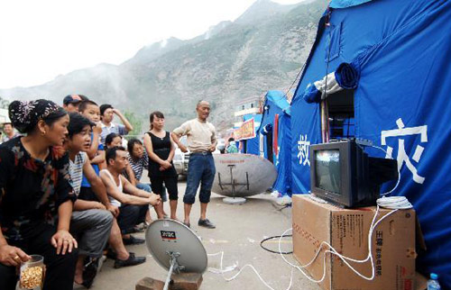 People watch TV outside a temporary tent in mudslide-hit Zhouqu county, Gannan Tibetan autonomous prefecture in Northwest China&apos;s Gansu province, August 12, 2010. [Xinhua]
