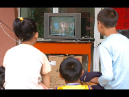 Children watch TV outside their temporary settlement in Zhouqu on Aug 16 as electricity supplies have been restored and 1,000 TV sets were installed in three settlements in Zhouqu on Monday[Xinhua]