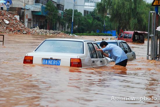 A passerby checks a car stranded on a flooded street in Kunming, capital of Yunnan province, to see whether there are people trapped, Aug 15, 2010. 