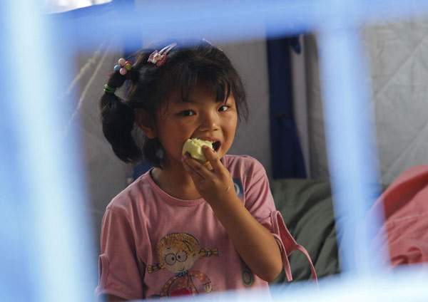 A girl eats an apple in a makeshift tent in mudslide-hit Zhouqu county, Northwest China&apos;s Gansu province, Aug 19, 2010. [Xinhua]