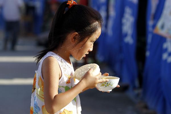  A girl walks to a tent with her food in the landslide-hit Zhouqu County, Gannan Tibetan Autonomous Prefecture in northwest China&apos;s Gansu Province, Aug. 19, 2010. [Xinhua]