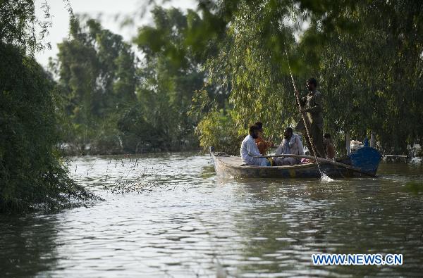 Flood refugees paddle a boat in water near Muzaffargarh, south Pakistan&apos;s Punjab Province, Aug. 23, 2010. [Xinhua]