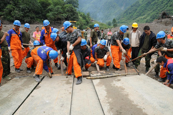 Workers lay steel plates on a bridge in Gongshan county, Southwest China&apos;s Yunnan province, Aug 24, 2010. The area&apos;s transportation resumed Tuesday after the road linking to the outside was cut off by a mudslide. As of 6:00 pm Monday, 32 people were dead and 60 others missing. [Xinhua]