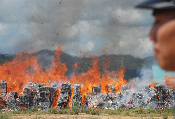 A policeman stands guard as boxes of fake cigarettes burn into ashes in Fuding, Southeast China&apos;s Fujian province, Aug 26, 2010. More than 3,800 boxes of fake cigarettes of 34 brands confiscated since Jan 2009 were destroyed in the event, Xinhua reported. [Xinhua]