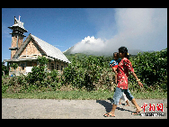 A woman carrying her child walks on the street at the district of Tanah Karo outside the city of Medan, North Sumatra, as Mount Sinabung volcano spews smoke in the background August 28, 2010. [Chihna Daily/Agencies]