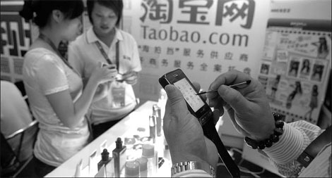 A taobao.com customer (right) shops online from his mobile phone. [China Daily]