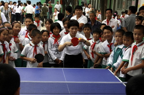 Deng Yaping shows students how to play ping-pong at the Huilei Primary School in Beijing on Sept 2, 2010.[Xinhua]