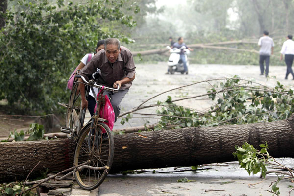 A girl helps an old man carry his bicycle across a tree blown down by a storm in Luoyang on Sept 4. Storms swept Luoyang, Central China&apos;s Henan province from 7 am Saturday. 15 villages have been hit by gales, hail and heavy rains. The bad weather left one person dead, and cut down electricity and telecommunication in some villages as well as destroying three bridges and blocking several roads, causing an estimated 900 million yuan ($132 million) in losses. [Xinhua] 
