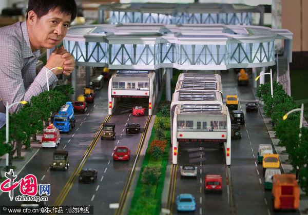 Song Youzhou, Chairman of Shenzhen Huashi Future Parking Equipment Co. Ltd. poses next to his invention, a scale model of &apos;straddle bus&apos;, at an office showroom in Beijing, Friday, Sept. 3, 2010. [CFP]