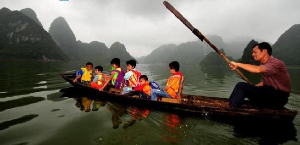 Shi takes his students to school on a wooden boat in South China's Guangxi Zhuang autonomous region on Sept 7, 2010. [Photo/Xinhua] 
