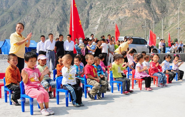 Kids and their parents attend an opening ceremony of a newly-built kindergarten for victims of mudslide-hit Zhouqu, Gansu province on September 14, 2010. The makeshift kindergarten serves as a simple but important education institution for kids of families in the disaster-battered area. [Photo/Xinhua]