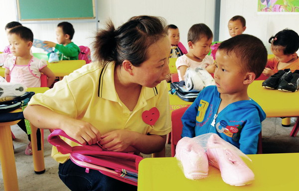 A teacher talks to a kid at a newly-built kindergarten for victims of mudslide-hit Zhouqu in Gansu province on September 14, 2010. [Photo/Xinhua] 