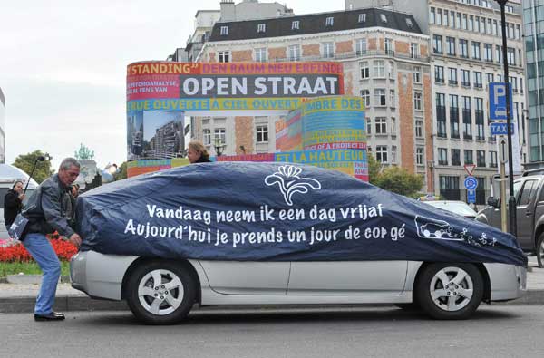 A man covers a car with a hood imprinted with the slogan of the car-free day, meaning “I’m on holiday today.” [Xinhua] 