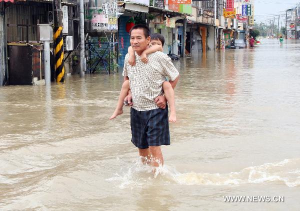 A man carrying a child on his back walks in floods in Tainan County, southeast China&apos;s Taiwan, Sept. 20, 2010. Typhoon Fanapi brought heavy rains and gales to southern Taiwan after it made landfall on Sunday, causing waterlog in some regions. A total of 12,000 residents have been evacuated. [Xinhua]