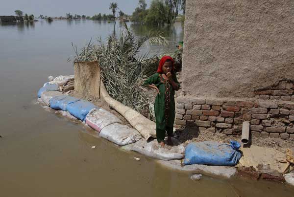 Momal, 7, displaced by flooding, stands on sand bags used as an embankment near her family house in the flooded town of Bobak, about 300 kilometres (186 miles) from Karachi on Sept 20, 2010. [China Daily/Agencies]