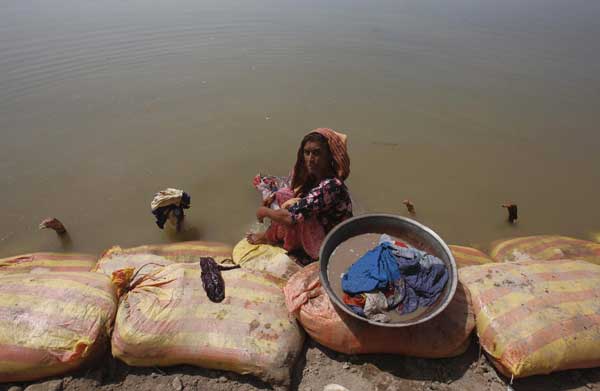 Razia, displaced by flooding, washes clothes in flood waters while sitting on sand bags in the town of Bobak. [China Daily/Agencies]