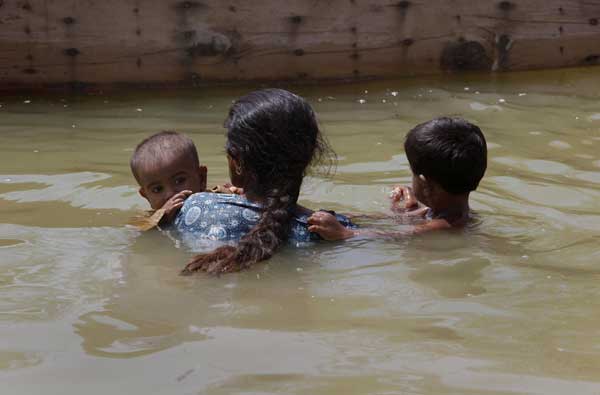 A woman displaced by flooding carries her children as she approaches a boat while returning to her flooded town of Bobak, about 300 kilometres (186 miles) from Karachi on Sept 20, 2010. [China Daily/Agencies]