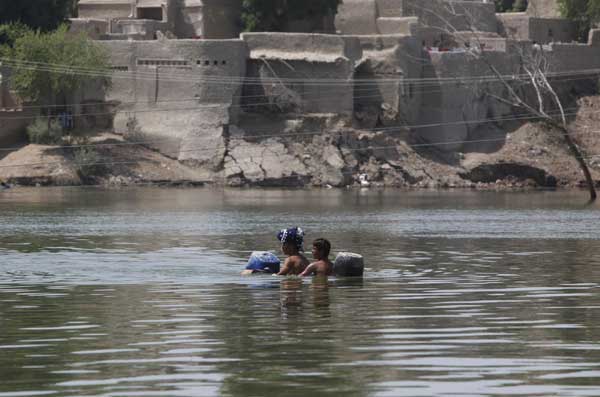 Villagers, displaced by flooding, use empty containers as a makeshift raft to transport them in flood waters as they return to their town of Bobak. [China Daily/Agencies]