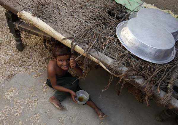 A child, displaced by flooding, sits under a rope bed at his flooded village in Dadu, some 320 km (198 miles) north of Karachi, Sept 20, 2010. [China Daily/Agencies]